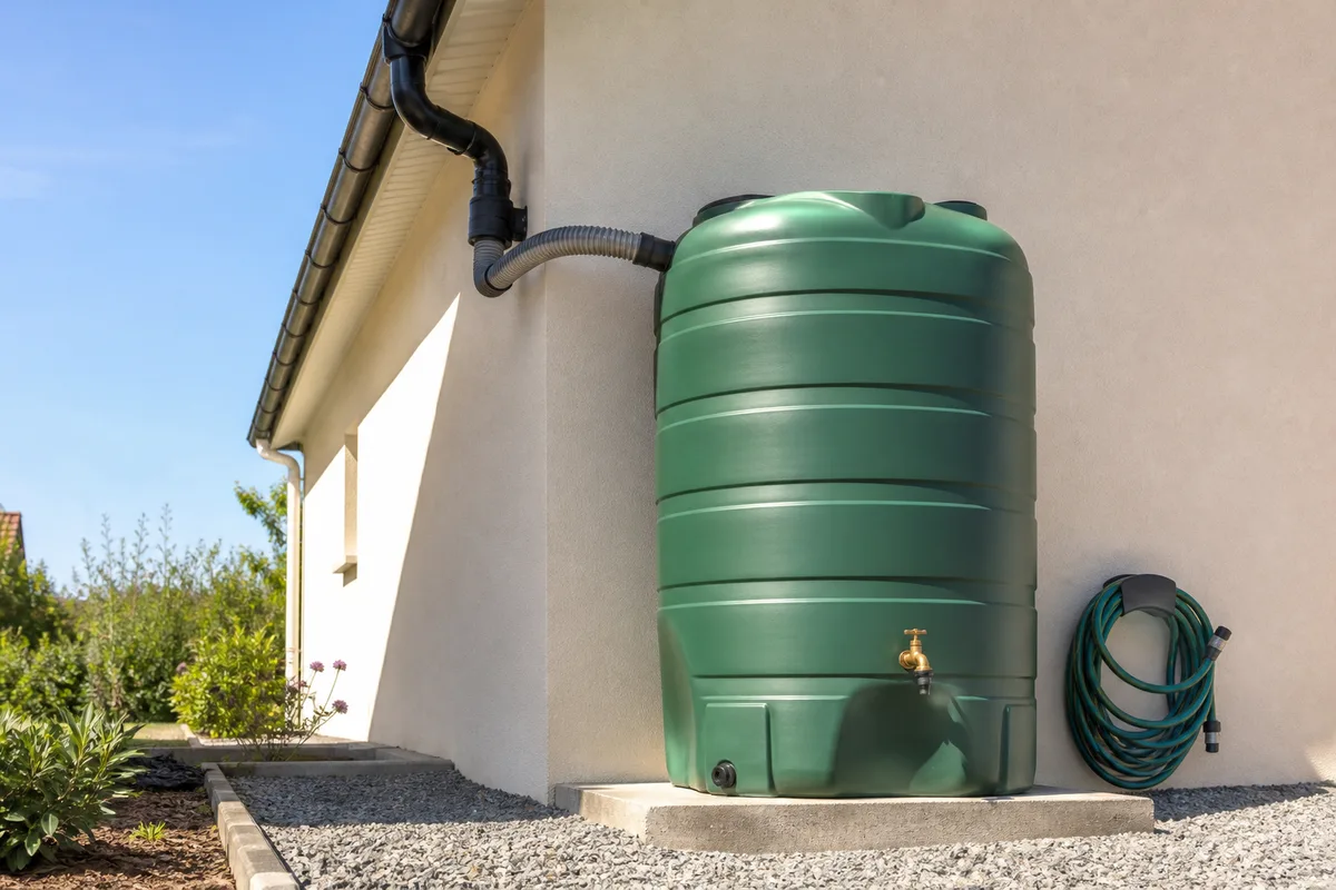 Cuve aérienne verte de mille litres installée le long d&rsquo;un mur de maison près d&rsquo;une descente de gouttière