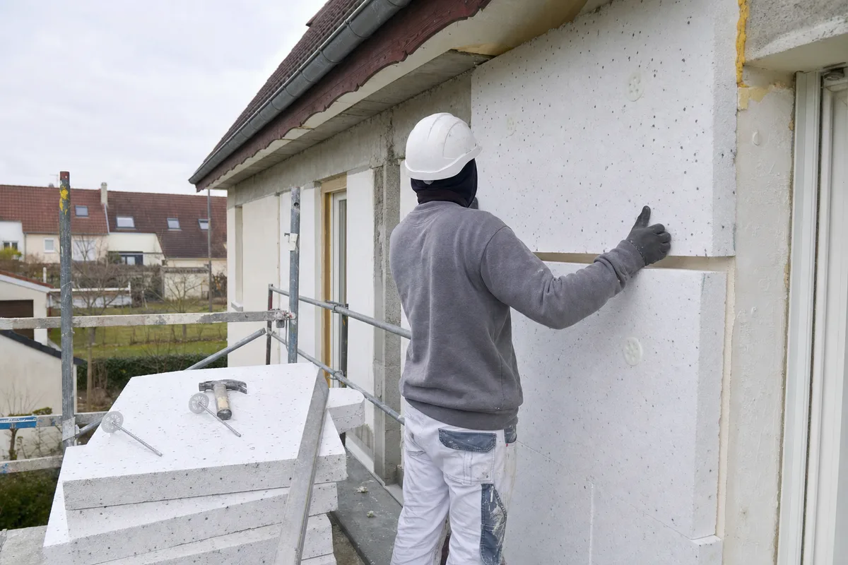 Ouvrier fixant un panneau isolant sur la façade d&rsquo;une maison en rénovation